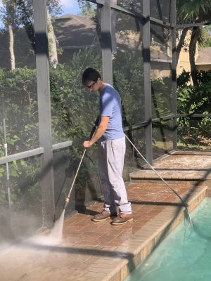 professional pressure washer washing pavers next to pool